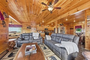 A log cabin interior with a dining area, two sofas, a coffee table, a ceiling fan, and a kitchen area. - Million Dollar Majestic View with best views around!!!! (Sevierville)