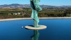 Eine Skulptur in einem Gewässer, im Hintergrund eine hügelige Landschaft.