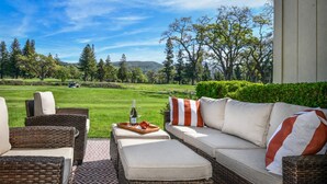 Ein Sitzbereich im Freien mit Korbmöbeln, einem Tisch mit Flasche und Gläsern sowie Blick auf einen Golfplatz.