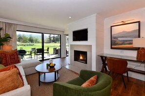 A modern living room with a fireplace, a television, and a view of a golf course.