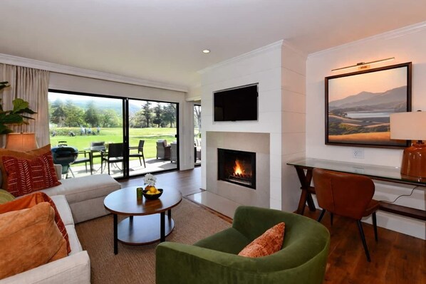 A modern living room with a fireplace, a television, and a view of a golf course. - Luxury stay,  views galore & pool. Walk to resort dining. (Napa)