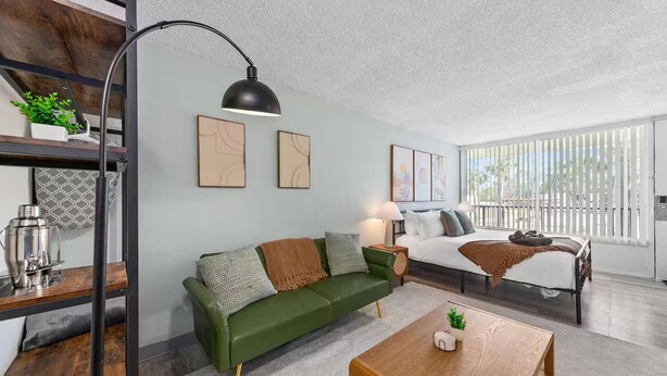Una sala moderna con un sofá verde, una mesa de centro de madera y una cama con vistas a un balcón.