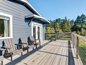 Eine Terrasse mit Adirondack-Stühlen, einem hölzernen Geländer und Blick auf Bäume.