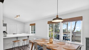 Una cucina moderna con una grande isola, sgabelli da bar e un'area pranzo con tavolo e sedie in legno.