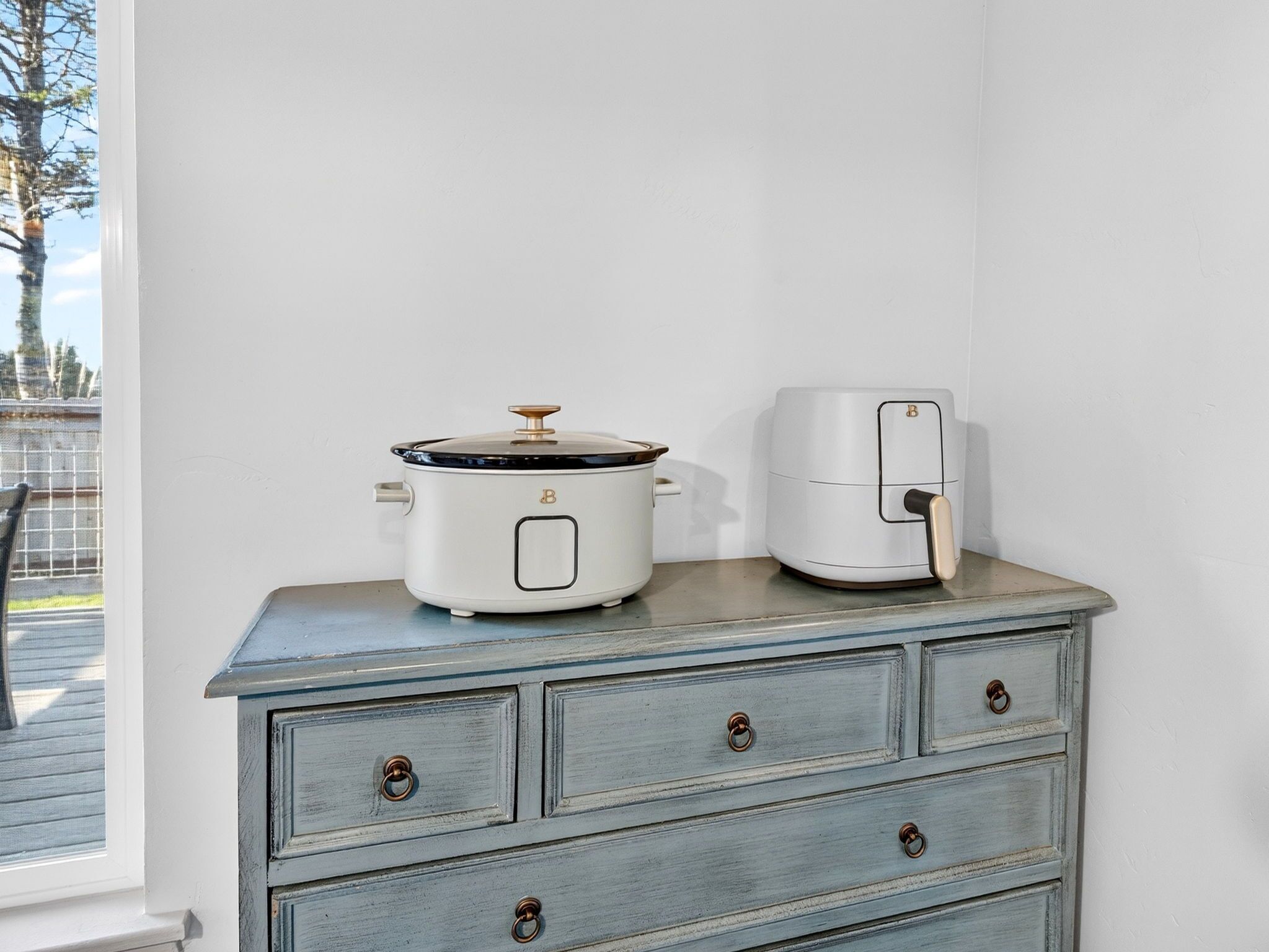 A kitchen with a white slow cooker and an air fryer on a wooden cabinet.