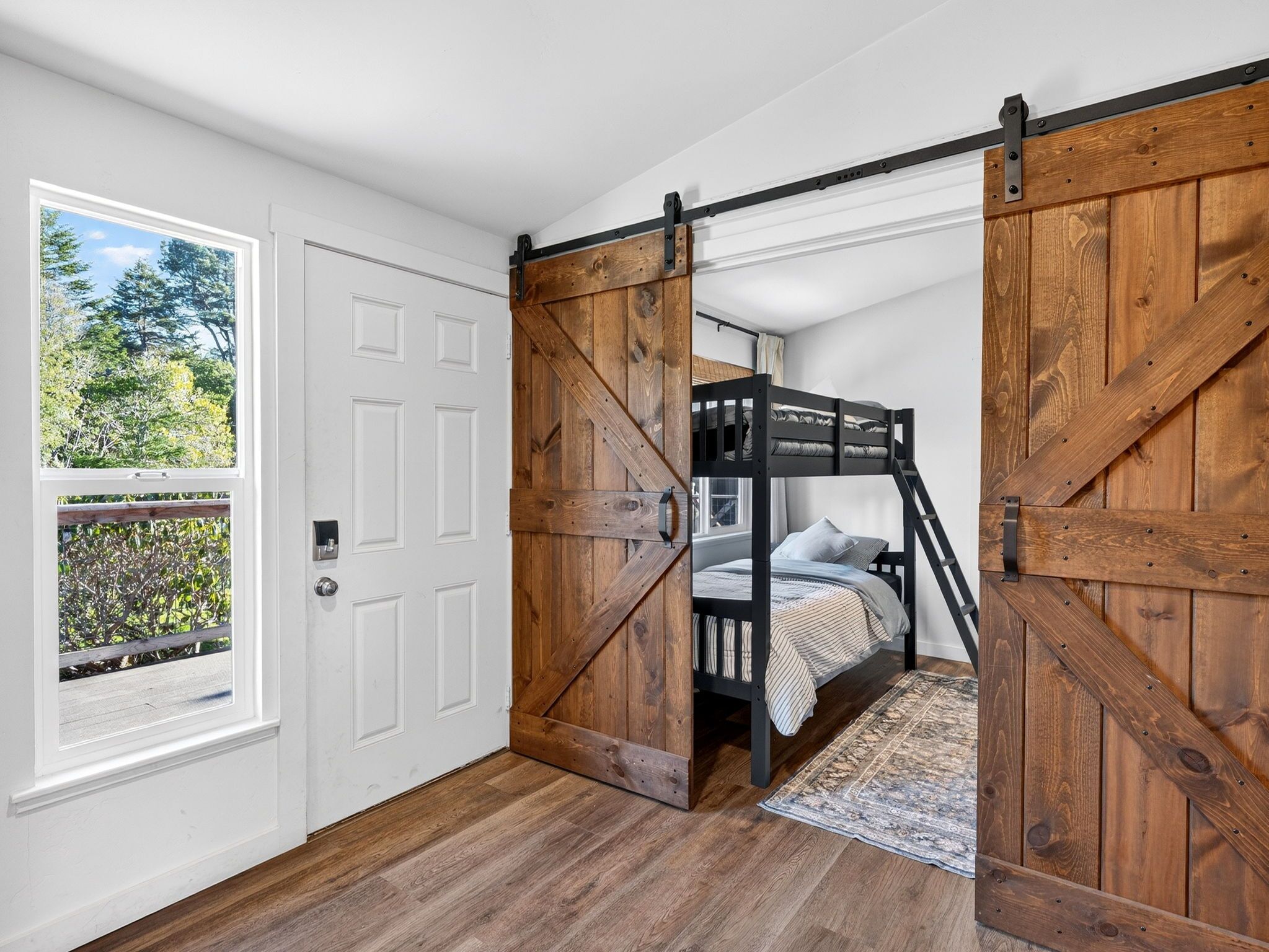 A bedroom with a bunk bed, a sliding barn door, and a view of the outdoors.