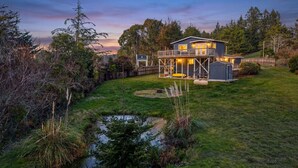 Una casa a due piani con un patio, uno stagno e vegetazione circostante.
