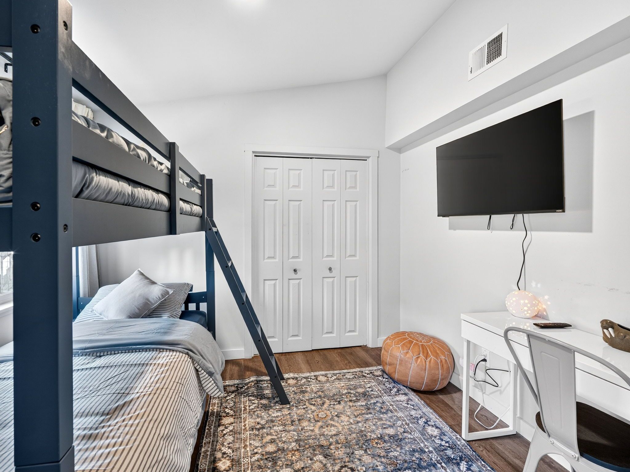 A bedroom with a bunk bed, a desk, a chair, a TV, and a patterned rug.