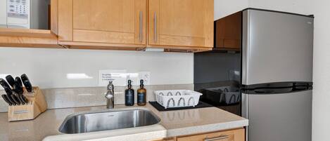 A kitchen with wooden cabinets, a stainless steel sink, a microwave, a refrigerator, and a knife block.