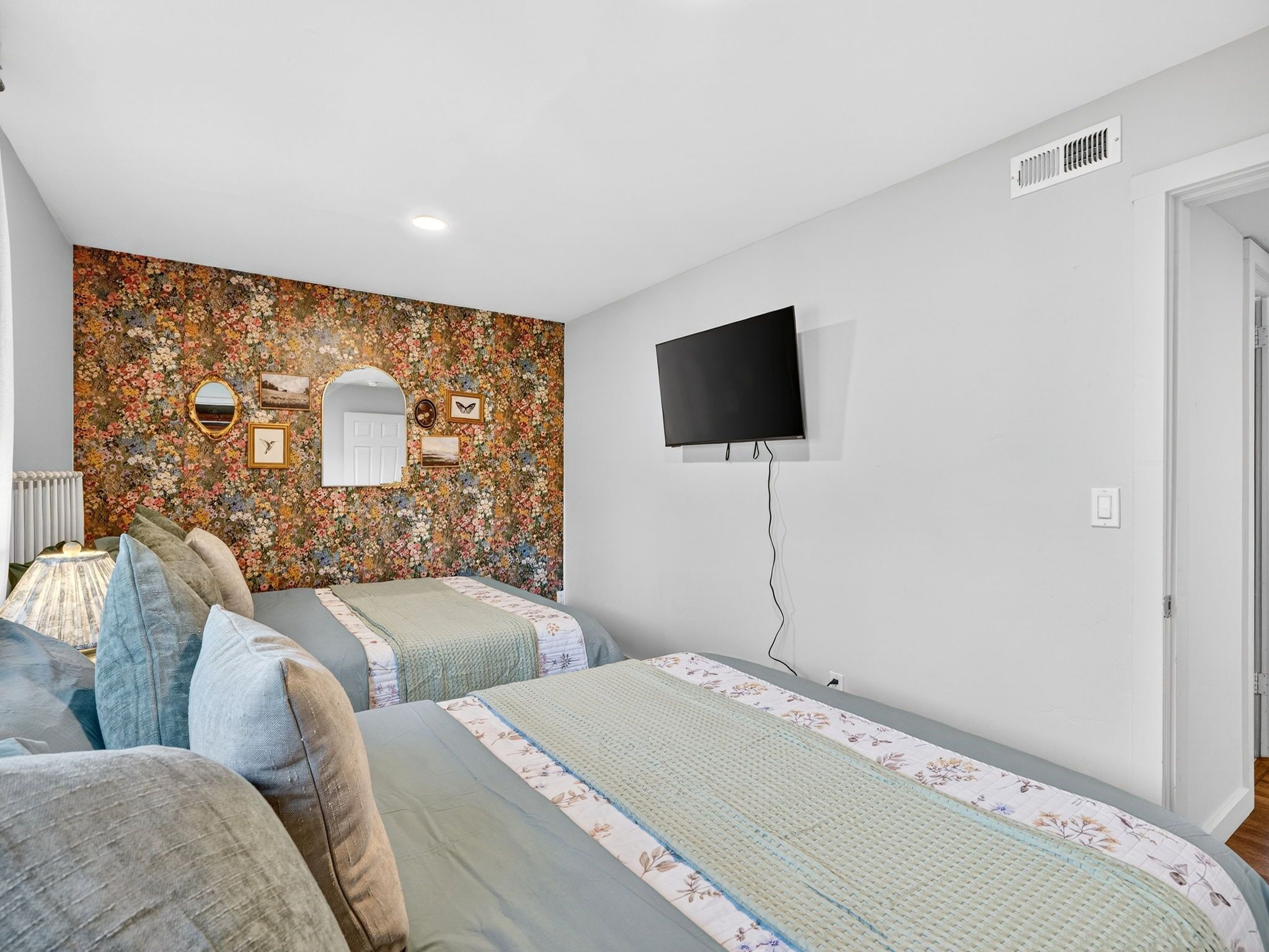 Un dormitorio con dos camas, televisión y un papel tapiz con estampado floral.