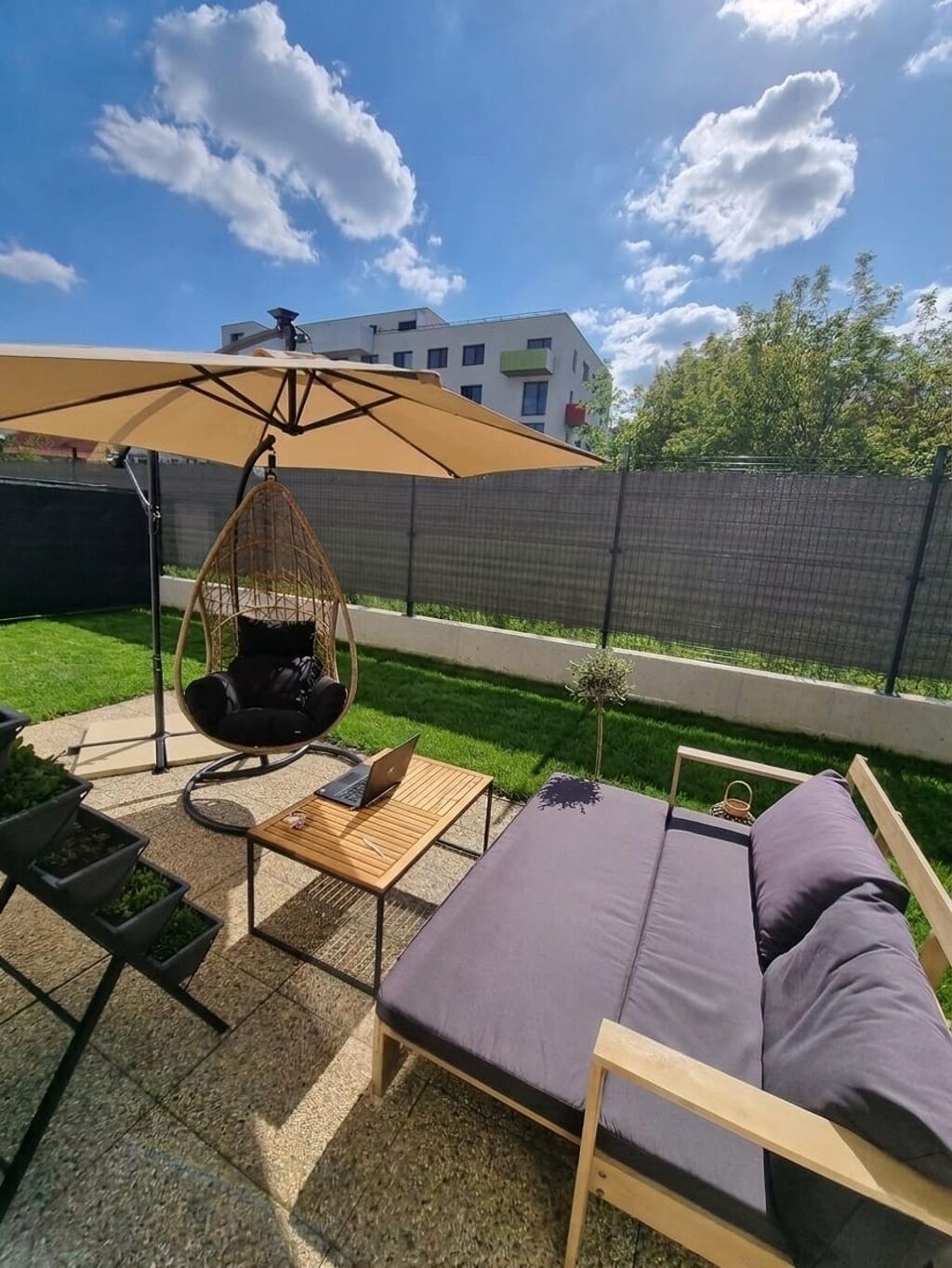 Un patio con una silla colgante, una mesa con una computadora portátil y un sofá.