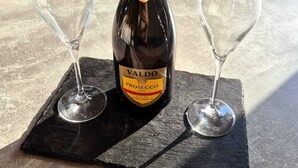 A bottle of Valdo Prosecco DOC on a black slate coaster with two empty wine glasses.