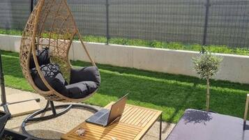 A patio with a hanging chair, a table with a laptop, and a cushioned bench.