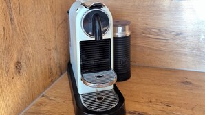 A Nespresso coffee machine on a wooden surface with a black coffee pod holder beside it.