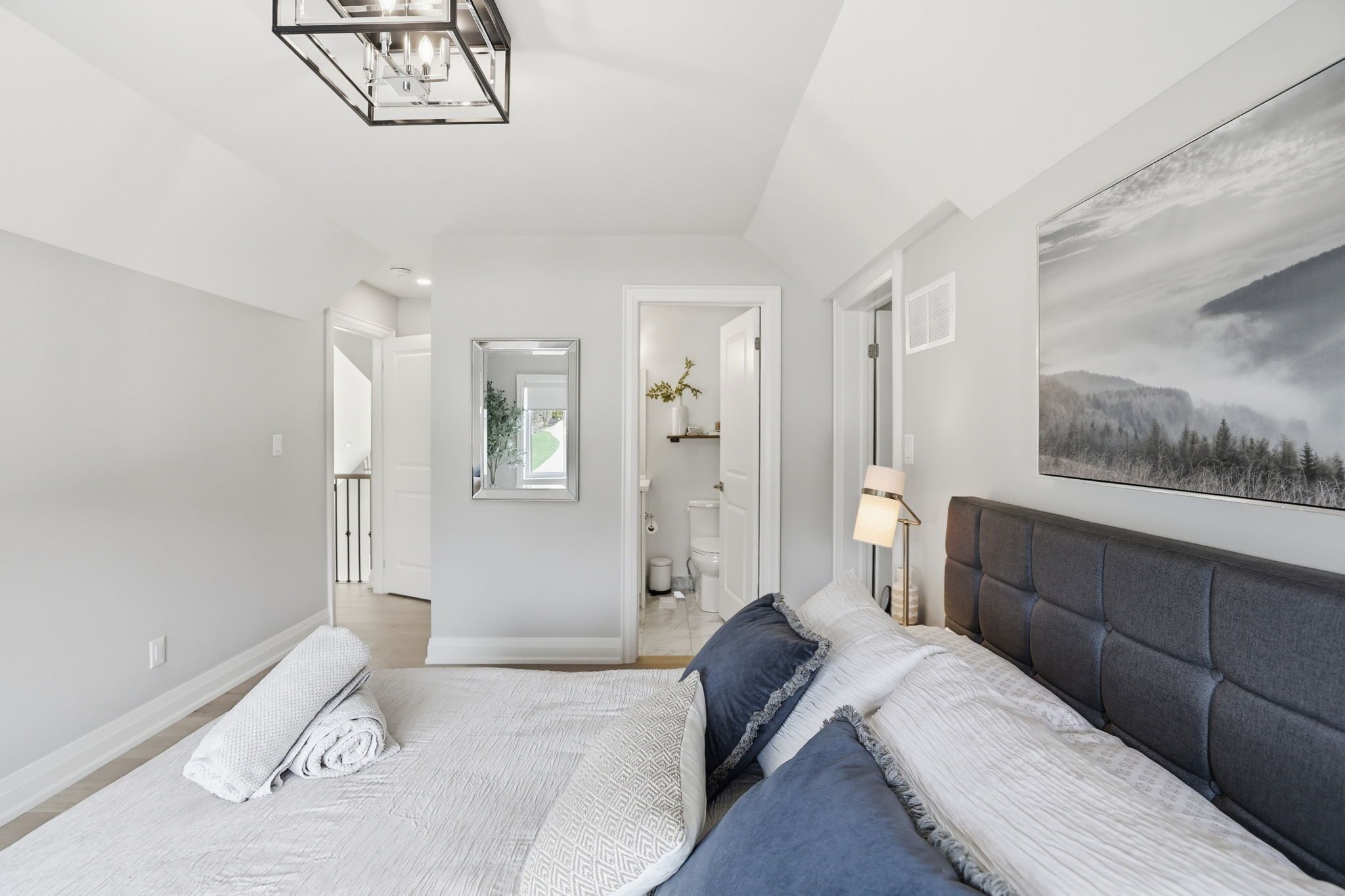 A modern bedroom with a large bed, a headboard, a mirror, and a painting on the wall.