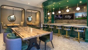 A modern bar area with a wooden bar counter, green upholstered bar stools, and pendant lighting. - Modern 1200sf 2bed apto in Frisco (Frisco)