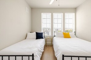 A room with two beds, white bedding, a small bedside table with a lamp, and a window with blinds. - Modern 1200sf 2bed apto in Frisco (Frisco)