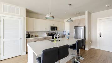 A modern kitchen with a central island, bar stools, stainless steel appliances, and pendant lighting.