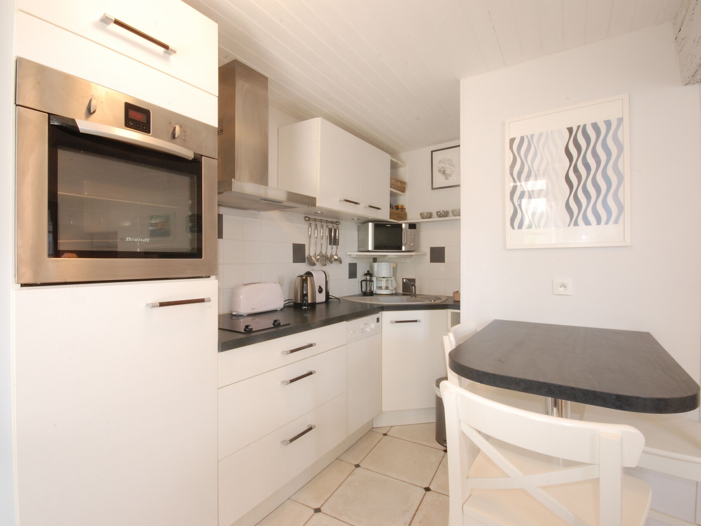 A modern kitchen with white cabinets, stainless steel appliances, a microwave, and a dining area with a table and chair.