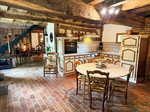 A rustic kitchen with exposed beams, a round dining table, and a staircase leading to another room. - Charming house with garden - 4 guests (La Fontenelle)