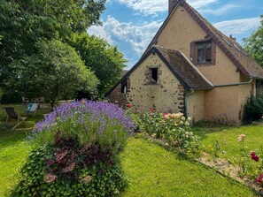 A rustic house with a thatched roof, surrounded by a garden with various flowers and a lawn. - Charming house with garden - 4 guests (La Fontenelle)