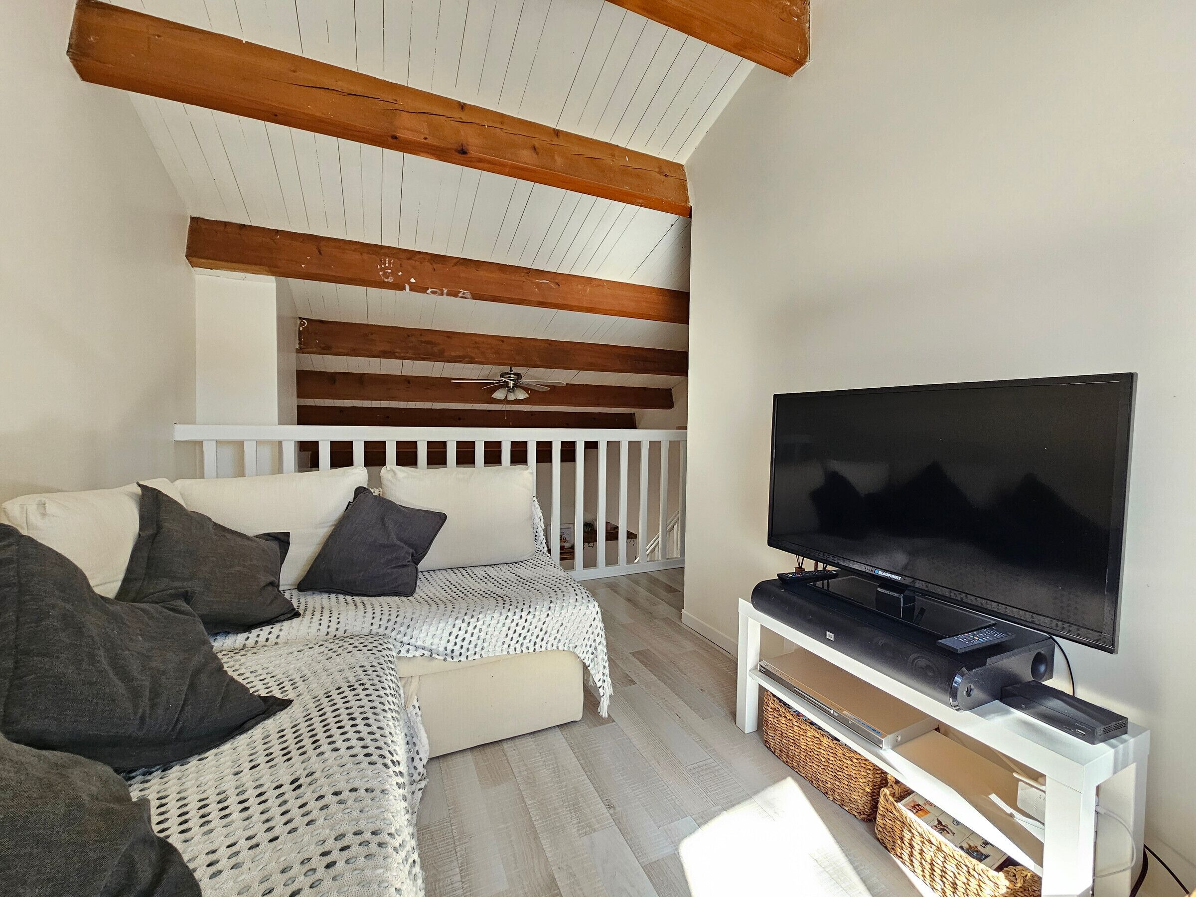 Un salon chaleureux avec un canapé blanc, un téléviseur à écran plat et des poutres en bois au plafond.