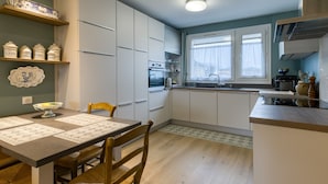 A modern kitchen with white cabinets, a wooden dining table, and a window providing natural light. - Apartmentby the sea - 4 guests (Châtelaillon-Plage)