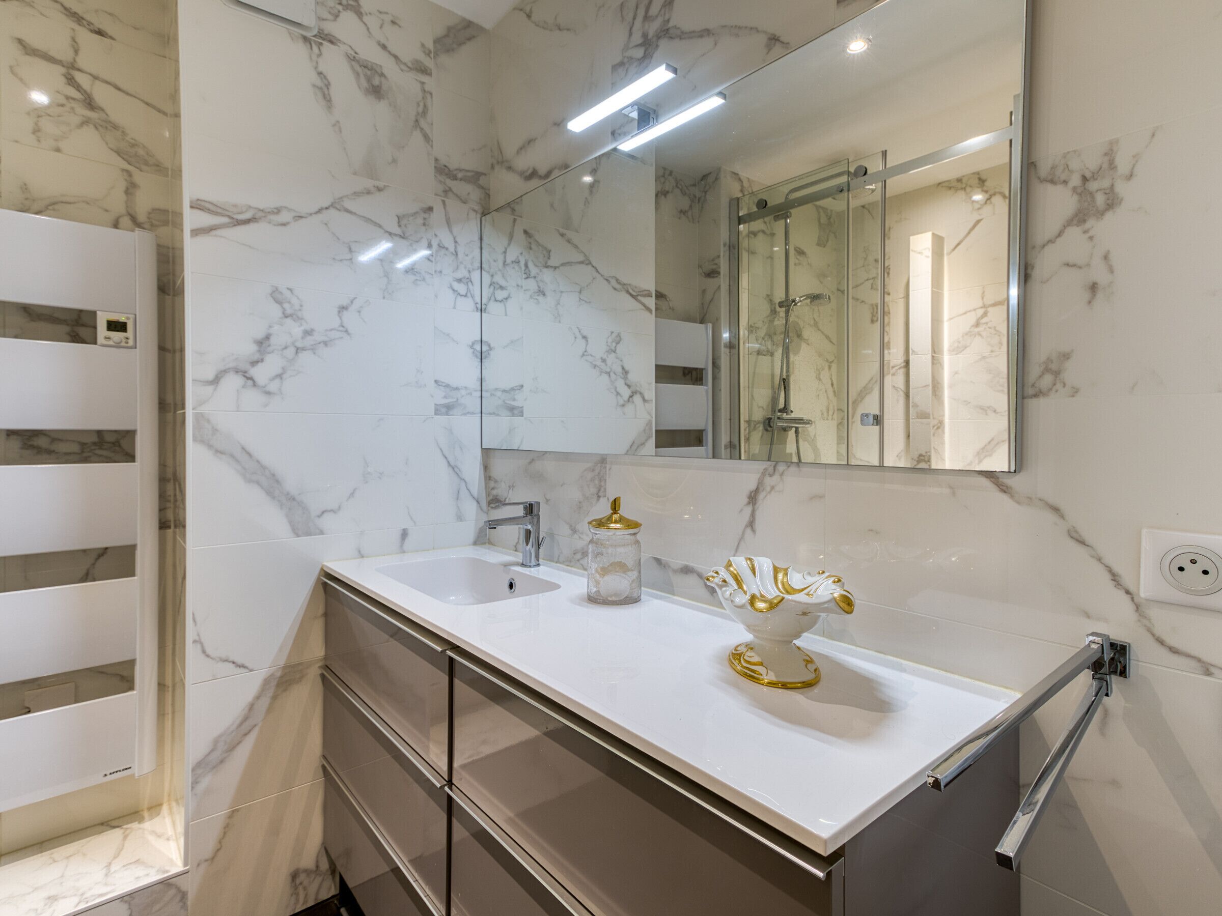A bathroom with marble walls, a white sink, a glass shower enclosure, and a large mirror.