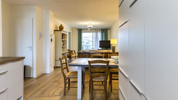 A compact kitchen with a dining area, wooden chairs, a white table, and a TV in the background. - Apartmentby the sea - 4 guests (Châtelaillon-Plage)