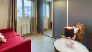 A modern room with a red sofa, a round marble table, a mirror, and a ceiling light fixture. - Apartmentby the sea - 4 guests (Châtelaillon-Plage)