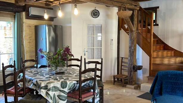 A rustic dining area with a table set for four, a wooden staircase, and a modern kitchen in the background. - Charming lodging with AC and parking - 4 guests (Corgnac-sur-l'Isle)