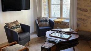 A living room with a flat-screen TV, two armchairs with patterned cushions, a wooden coffee table with glasses, and a stone-patterned wall. - Charming lodging with AC and parking - 4 guests (Corgnac-sur-l'Isle)