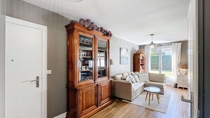 A spacious living room with a wooden cabinet, a beige sofa, and a dining table. - Ground floor apartment, near the sea (Jullouville)
