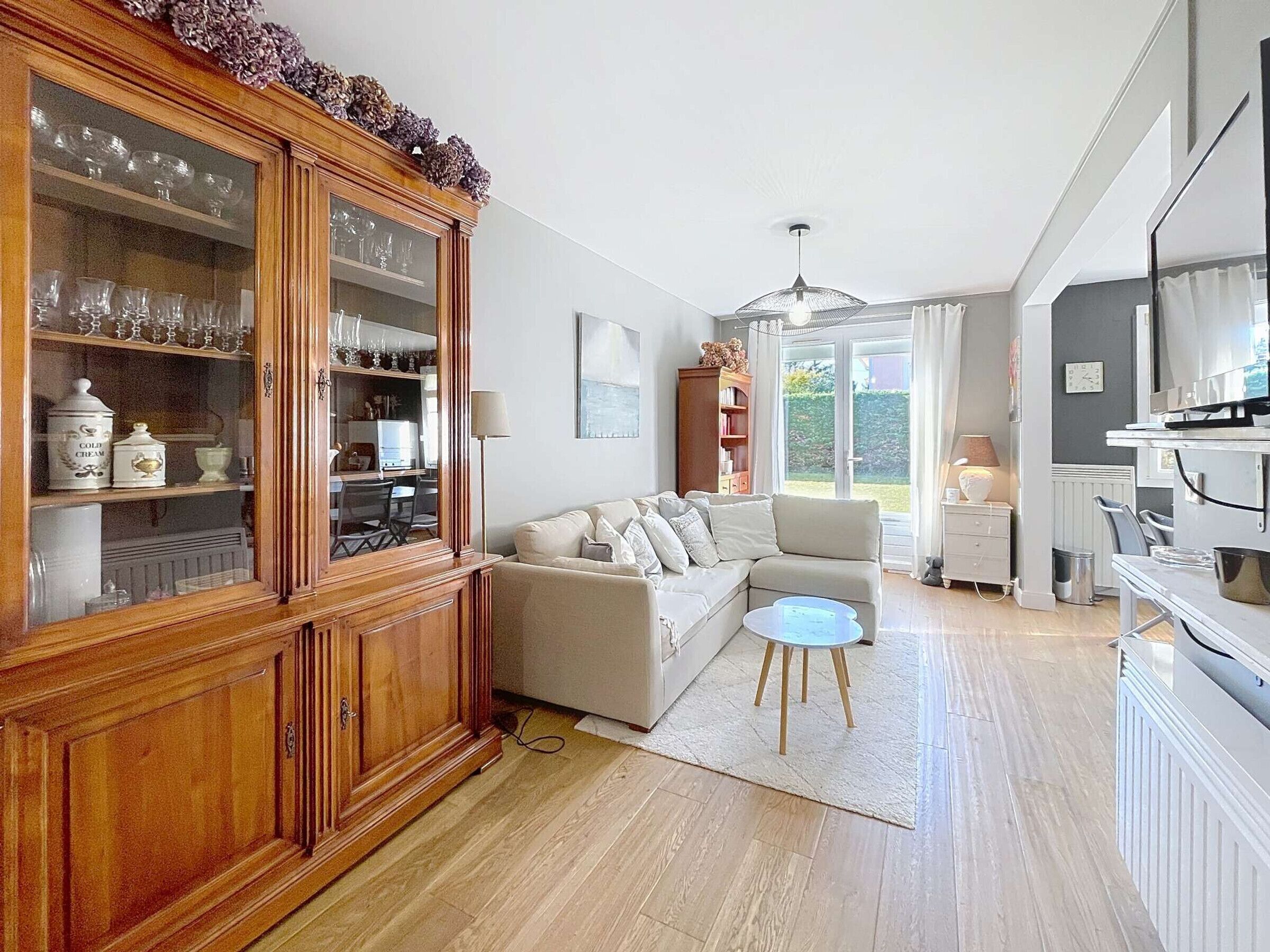A spacious living room with a wooden cabinet, a beige sofa, a small round table, and a kitchen area with a TV.