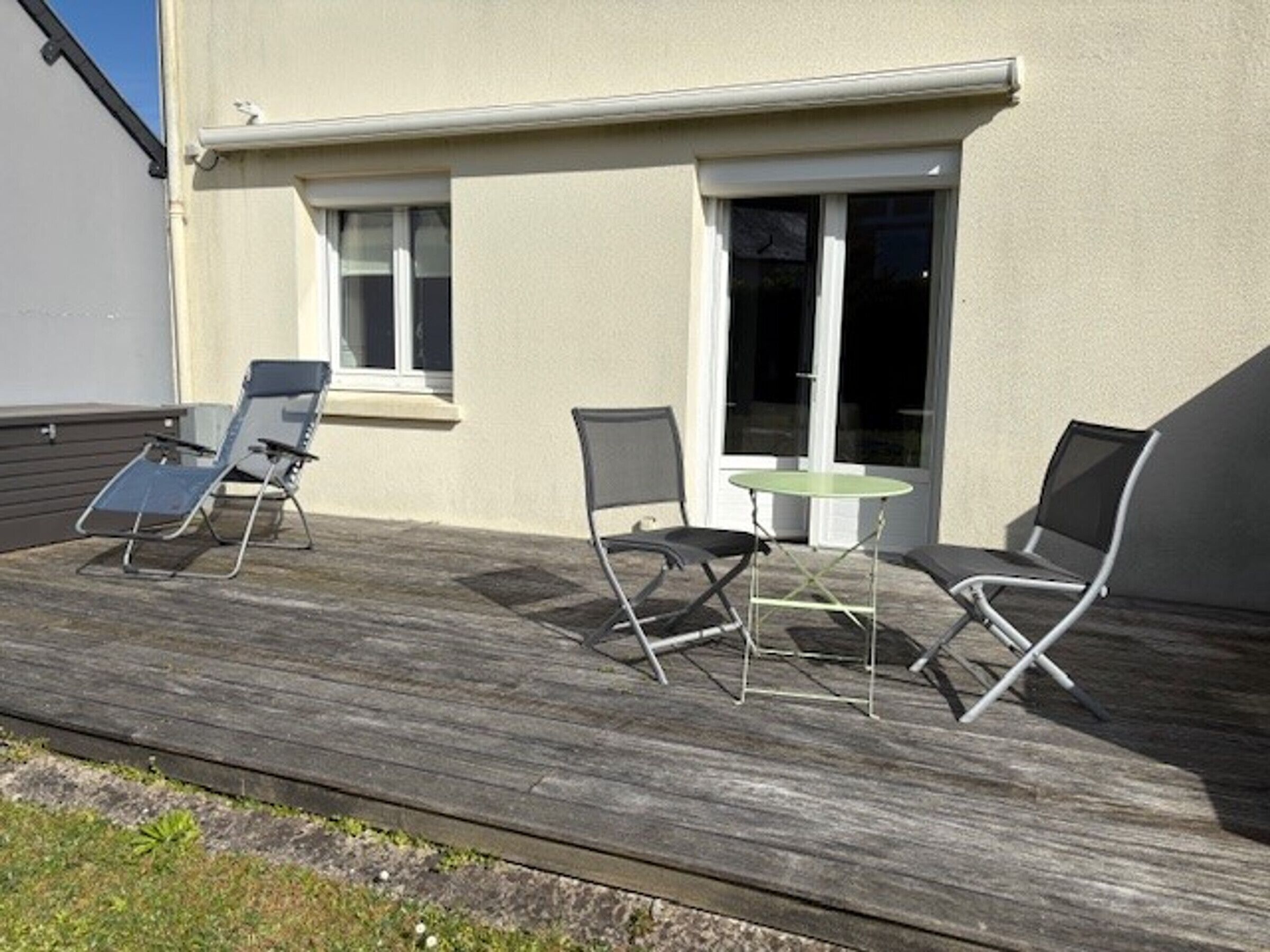 Eine Terrasse mit drei Stühlen, einem Tisch, einem Fenster und einer Tür.