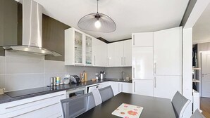 A modern kitchen with white cabinets, a black countertop, and a central island with chairs. - Ground floor apartment, near the sea (Jullouville)