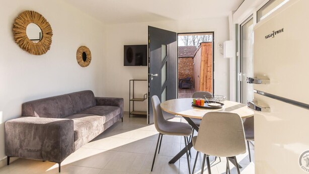 Una sala de estar moderna con un sofá, una mesa de comedor con sillas, un televisor y una puerta que da a un área exterior.