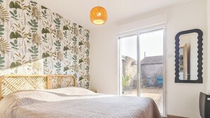 Un dormitorio con cama, una ventana grande y una pared con diseño de hojas.