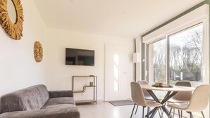 Una sala moderna con un sofá, un televisor montado en la pared y un comedor con sillas y una mesa.