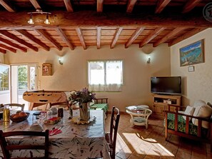 A cozy living room with a wooden ceiling, a dining table with chairs, a TV, and a window with curtains. - Spacious gîte near nature - 10 guests (Chavanay)