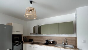 A modern kitchen with white cabinets, a built-in oven, a coffee maker, and a pendant light. - Spacious apartment with large terrace - 4 guests (Aix-les-Bains)