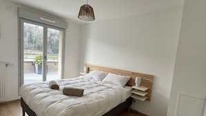 A bedroom with a bed, a bedside table, a hanging light fixture, and a sliding glass door leading to an outdoor area. - Spacious apartment with large terrace - 4 guests (Aix-les-Bains)