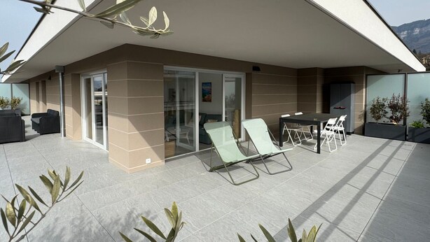 A modern outdoor patio with a glass enclosure, seating, and potted plants. - Spacious apartment with large terrace - 4 guests (Aix-les-Bains)