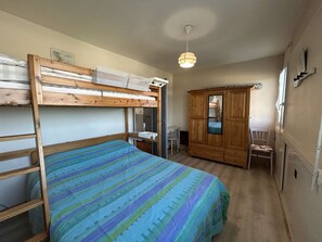 Una cama litera con colcha a rayas, un armario de madera, un escritorio con silla y una lámpara colgante.
