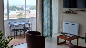 Une pièce comprenant une table à manger, des chaises, un téléviseur, un radiateur et une vue sur la ville.