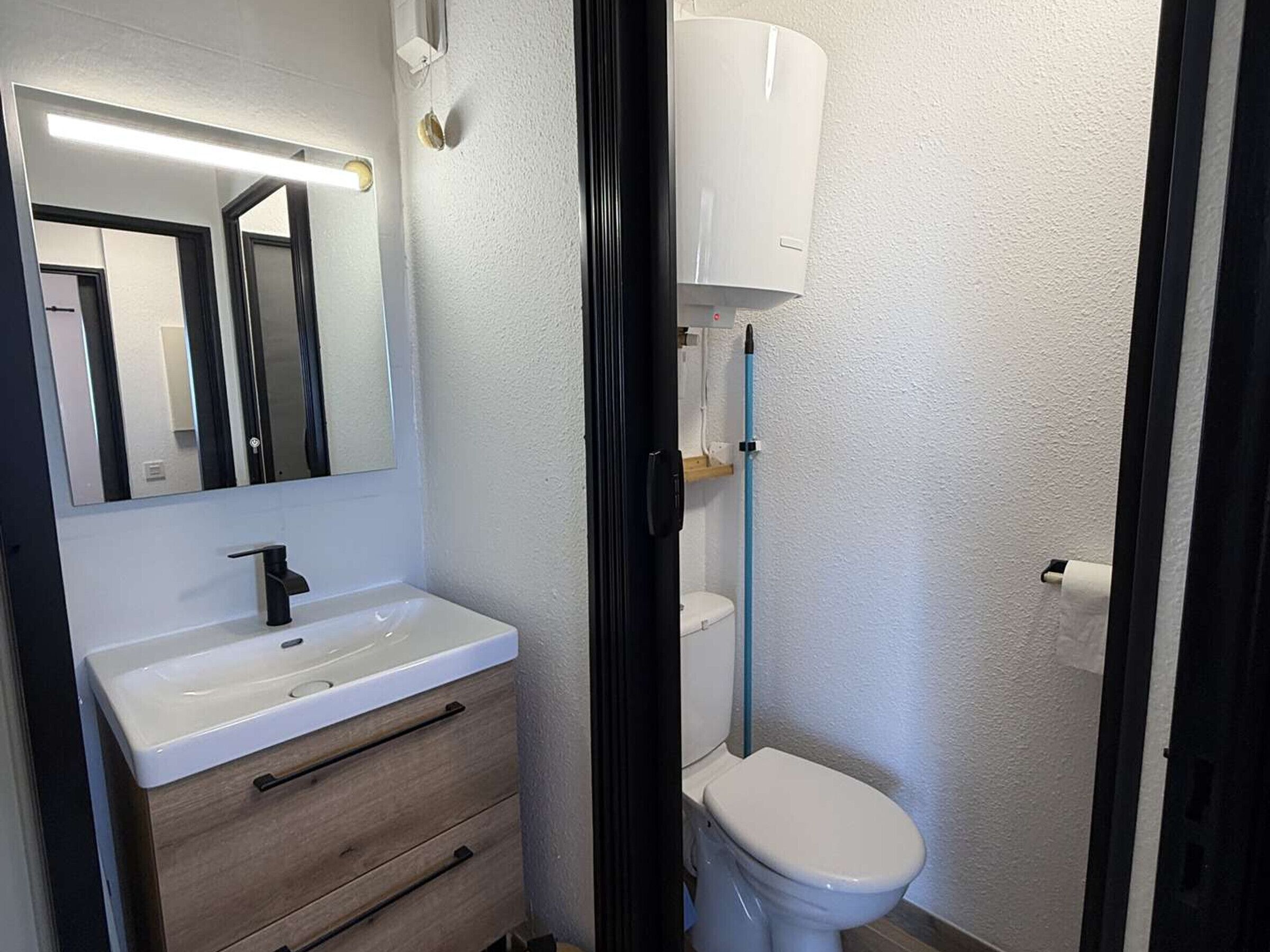 A bathroom with a white sink, a mirror, a toilet, and a blue cleaning pole.