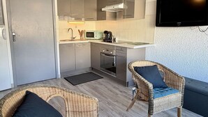 Cozinha compacta com eletrodomésticos modernos, uma TV de tela plana e cadeiras de vime.