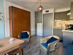 A compact kitchen with a dining area, wicker chairs, a wooden table, and a hanging light fixture. - Cozy studio, private parking - 3 guests (Gruissan)