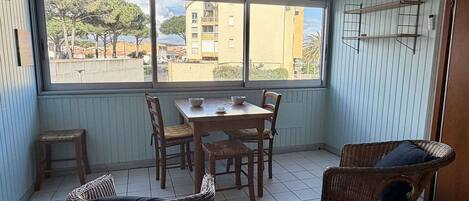 A dining area with a table and chairs, a window with a view of buildings, and a shelf with items.