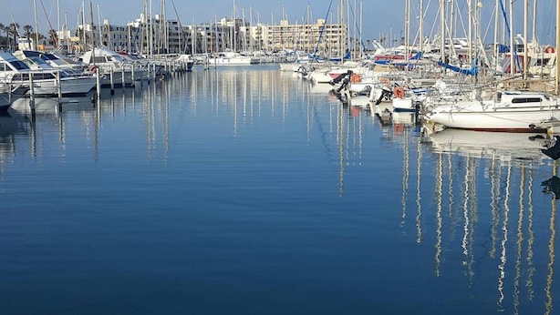 Ein Yachthafen mit mehreren angedockten Booten, ruhigem Wasser und Gebäuden im Hintergrund.